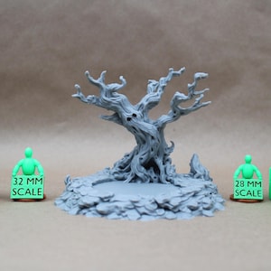 May include: A gray 3D printed miniature of a gnarled, leafless tree with a face, set on a rocky base. It is flanked by two green figures holding signs labeled 32 MM SCALE and 28 MM SCALE, alongside stacked brown and green 25 MM CUBE blocks.