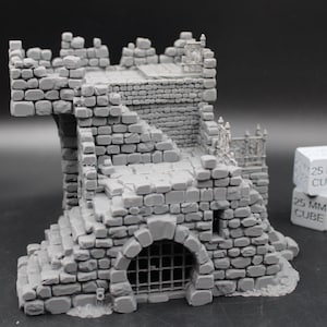 May include: A gray miniature stone fortress structure featuring a vaulted archway with a metal-style grate, a raised platform with battlements, and stone stairs. Next to the structure are two stacked white cubes labeled 25 MM CUBE.