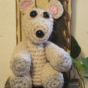May include: A crocheted plush toy bear with a light brown body, pink ears, and black eyes. The bear is sitting on a small wooden stool painted blue with gold accents.