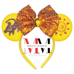 May include: Yellow mouse ears headband with a large orange and gold sequin bow. The ears feature a brown and gold lion silhouette on one ear and a gold sun on the other. The headband has the text "MAGIC MERCH ACCESSORIES" printed on it.
