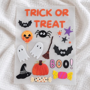 Könnte beinhalten: Ein transparenter Bogen mit Halloween-Aufklebern, der den orangefarbenen Schriftzug TRICK OR TREAT und das Wort BOO in Pink und Schwarz enthält. Die Aufkleber zeigen eine schwarze Fledermaus, einen Kürbisballon, eine Spinne, einen Besen, zwei weiße Geister, einen Hexenhut, einen Kürbis, Sterne und Süßigkeiten.