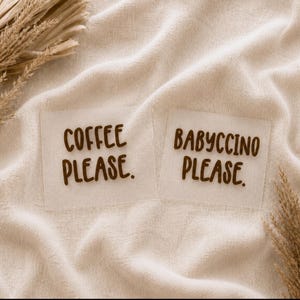 Puede incluir: Dos pegatinas cuadradas de color blanquecino con texto marrón. Una dice "COFFEE PLEASE." y la otra dice "BABYCCINO PLEASE." Las pegatinas están sobre una tela beige texturizada, con plantas secas en las esquinas.
