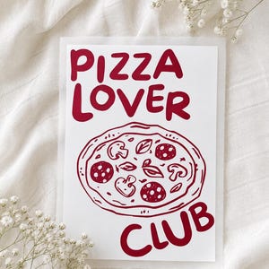 Könnte beinhalten: Eine rechteckige weiße Grußkarte mit dunkelrotem Text, der PIZZA LOVER CLUB lautet. Unter dem Text befindet sich eine dunkelrote Strichzeichnung einer Pizza, die mit Pilzen, Salamischeiben und Basilikumblättern belegt ist.
