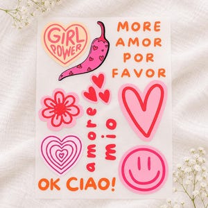 May include: A sticker sheet featuring various designs including a pink chili pepper with hearts, a red flower, a pink heart, a smiley face, and text that reads Girl Power, More Amor Por Favor, Amore Mio, and OK CIAO! in orange and red colors.
