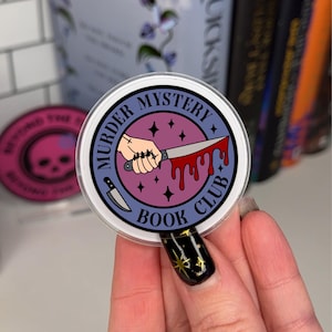 Op de afbeelding: Ronde sticker met de tekst "MURDER MYSTERY BOOK CLUB". De sticker toont een hand die een bloedig mes vasthoudt, tegen een paarse en roze achtergrond, met een kleine mesafbeelding.