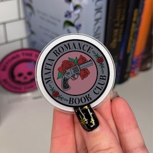 Puede incluir: Una pegatina redonda con fondo gris y texto blanco que dice "Mafia Romance Book Club". La pegatina presenta un círculo rosa con un revólver negro y gris y rosas rojas.