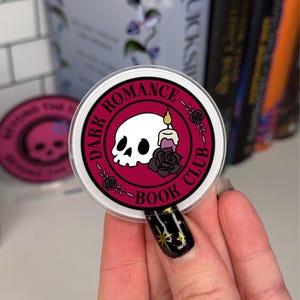 Peut inclure: Un autocollant rond avec un crâne blanc et une bougie allumée sur un fond rouge. Le texte "DARK ROMANCE BOOK CLUB" est écrit dans un cercle noir autour du crâne et de la bougie.