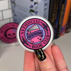Peut inclure: Un autocollant rond rose et violet avec le texte "Antisocial Book Club" et un livre fermé avec le texte "Fuck off I'm reading".