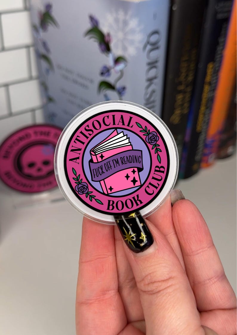 K&ouml;nnte beinhalten: Ein runder Aufkleber in Pink und Lila mit dem Text "Antisocial Book Club" und einem geschlossenen Buch mit dem Text "Fuck off I'm reading".