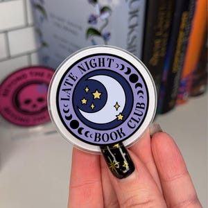 May include: A purple and white sticker with a crescent moon and stars. The sticker says "Late Night Book Club" in a circle around the moon.