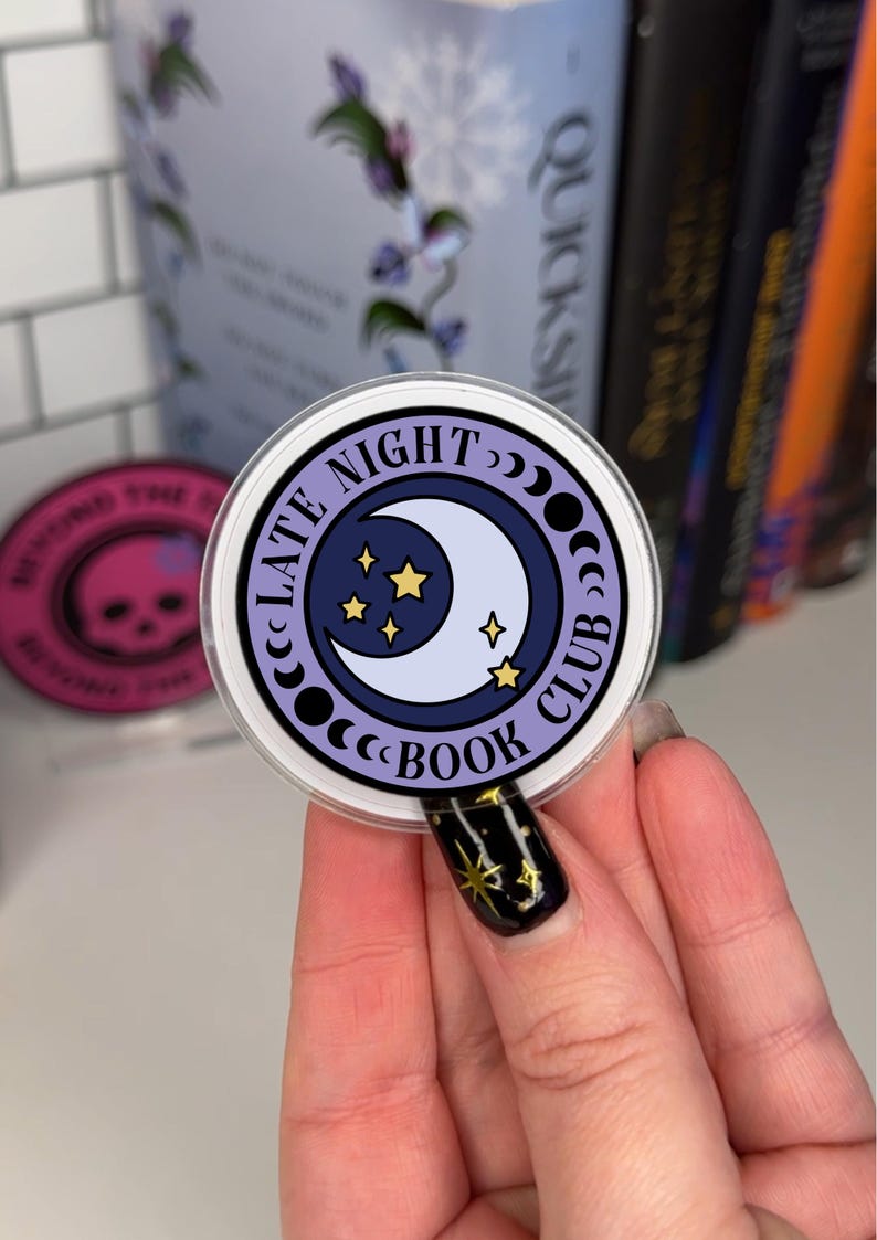 May include: A purple and white sticker with a crescent moon and stars. The sticker says "Late Night Book Club" in a circle around the moon.