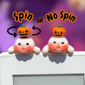 May include: Two small white ghost figurines with rosy cheeks and black eyes, each topped with a miniature orange jack-o'-lantern. The left ghost has curved arrows indicating rotation, and the text above reads Spin OR No Spin.