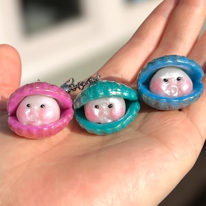 May include: Three small pearl-like charms with faces, each inside a different colored seashell: pink, teal, and blue.