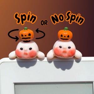 May include: Two small white ghost figurines with pink cheeks and black eyes, each topped with a miniature orange jack-o'-lantern. The text Spin or No Spin appears above them, with curved arrows indicating rotation for the left ghost figurine.