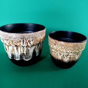 Peut inclure: Deux pots de fleurs en céramique de tailles différentes, présentant tous deux un intérieur noir foncé et une base qui se transforme en un motif d'émail texturé de style goutte à goutte dans des tons crème, beige et marron.