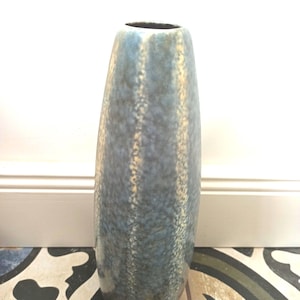 Op de afbeelding: Een hoge, blauwe keramische vaas met een gespikkelde textuur. De vaas heeft een licht uitlopende bovenkant en een afgeronde body. De kleur is een mix van blauw en beige. De vaas is ongeveer 30 cm hoog.