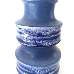 Puede incluir: Un jarrón de cerámica azul con un diseño texturizado y en capas. El jarrón tiene una base ancha y una parte superior más estrecha, con una banda texturizada y moteada de blanco en el medio. El jarrón mide unos 25 cm de alto.