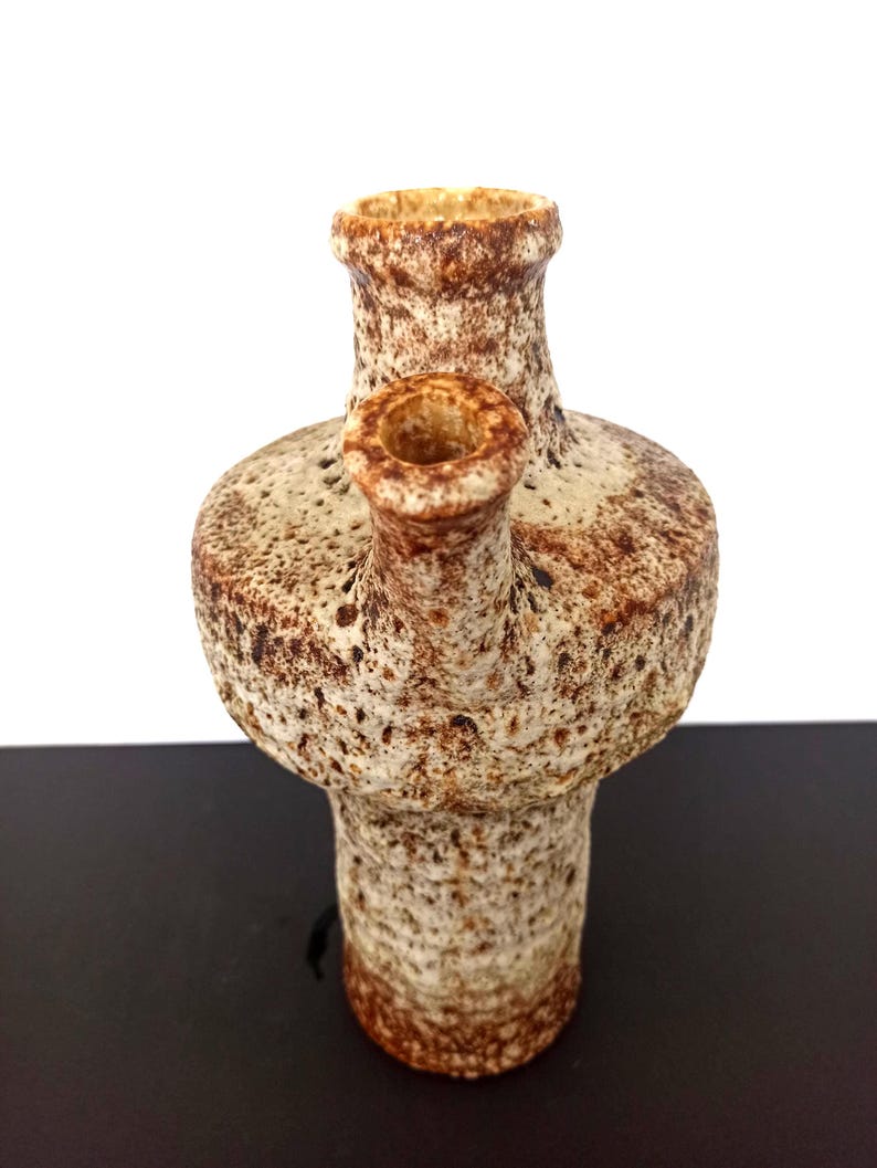 May include: A textured ceramic vase with a unique design. The vase has a light beige base color with brown speckles and accents. It features a cylindrical neck and a smaller spout on the side. The vase is approximately 7 inches tall.