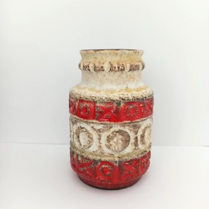 Può includere: Un vaso in ceramica bianco e rosso con un motivo geometrico. Il vaso ha un corpo arrotondato e una parte superiore leggermente svasata.