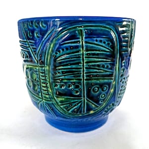 Può includere: Un vaso in ceramica caratterizzato da una smaltatura blu vivace e verde intenso. La superficie esterna è decorata con un motivo in rilievo composto da linee verticali, punti circolari e forme geometriche astratte che avvolgono il vaso.