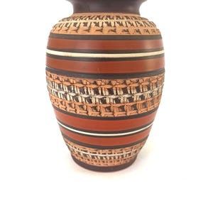 May include: A decorative ceramic vase with a textured surface and a brown, orange, and white color scheme. The vase features horizontal stripes and a patterned design, suitable for home decor.