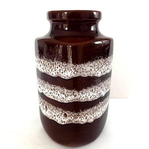 May include: A dark brown ceramic vase with a glossy finish, featuring three horizontal bands of textured, foamy white glaze that wrap around the cylindrical body. The vase has a short, narrow neck and a wide, rounded base with a smooth surface.