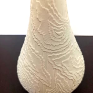May include: Cream-coloured ceramic vase with a textured, topographic design. The vase has a rounded base that tapers to a narrower neck. The surface features a raised, layered pattern, creating a unique visual and tactile experience. The vase is likely for decorative purposes.