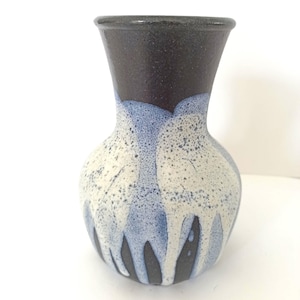 Könnte beinhalten: Eine kleine, runde Keramikvase mit einer dunkelbraunen Glasur an der Oberseite, die in eine weiße Glasur mit blauen Akzenten und Sprenkeln übergeht. Die Vase hat einen schmalen Hals und einen breiten Boden.