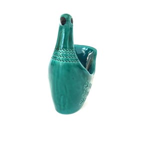 May include: A teal blue ceramic bird-shaped vase with a textured design. The vase is a decorative piece for the home.