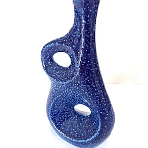 May include: A dark blue ceramic vase with a speckled pattern. The vase has a unique design with two circular openings. The vase is a decorative item, suitable for displaying flowers or as a standalone art piece.