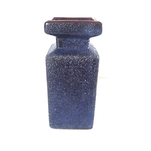 Puede incluir: Un jarrón azul oscuro con una superficie texturizada y una parte superior cuadrada. El jarrón tiene un cuerpo cilíndrico y un aspecto moteado. El interior es de color marrón oscuro. Un diseño moderno adecuado para varios estilos de decoración.