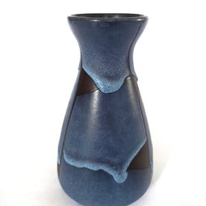 May include: A blue ceramic vase with a dark brown accent. The vase has a unique shape, with a narrow neck and a wider body. The blue glaze has a dripped effect, adding visual interest. The vase is set against a white background.