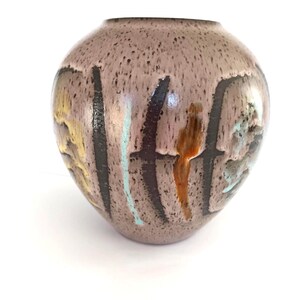May include: A round, speckled vase with a wide opening. The vase is primarily a muted mauve color, with vertical black, yellow, and teal accents. The vase has a glossy finish and is set against a white background.