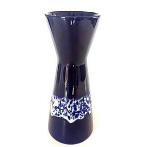 Peut inclure: Un vase en céramique bleu marine avec un haut et une base évasés, et une taille étroite. La partie inférieure présente un motif abstrait blanc et moucheté. Le vase a une finition brillante et se détache sur un fond blanc.