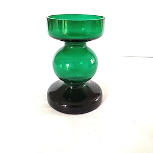 May include: A green glass candle holder with a unique hourglass shape. The top and middle sections are a vibrant green, while the base is a darker shade of green. This decorative piece is ideal for adding a touch of color to any room.
