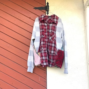 May include: A red and black plaid shirt with grey and white striped sleeves hanging on a hook against a red and white wall.