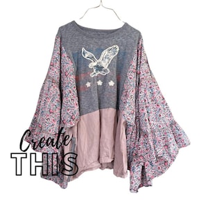 Może przedstawiać: Szara, różowa i kwiatowa bluzka z grafiką orła. Top ma długie, rozkloszowane rękawy z kwiatowym wzorem i napis "Create THIS" czarną kursywą.