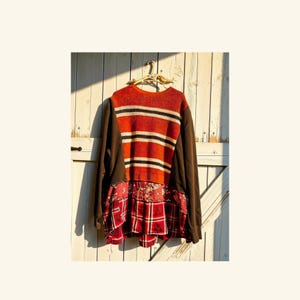 May include: A long-sleeve pullover featuring a knit orange, black, and white striped upper section, solid brown sleeves, and a lower panel with a red plaid pattern and a floral print. The word "Bed" is embroidered in light thread on the front.