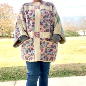 May include: A white quilted jacket with floral patchwork and two pockets. The jacket has a relaxed fit and is made of a soft, comfortable fabric.