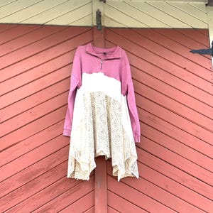 以下が含まれることがあります： モーヴと白の長袖トップス、クォータージップのネックライン、クリーム色のレーススカート。赤い木の表面にトップスが掛かっています。