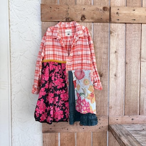 May include: A long-sleeved button-down shirt featuring a red and white plaid pattern on the upper portion. The lower section is constructed from contrasting fabric panels, including a black floral print, a dark green ruffle, and a white floral print.