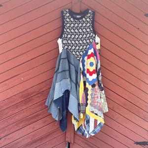 May include: A sleeveless dress featuring a black and white patterned knit bodice. The skirt is constructed from a combination of blue denim fabric panels and a multi-colored patchwork quilt section with hexagonal patterns in red, yellow, and blue.