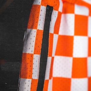 May include: Orange and white checkered fabric with a black zipper detail. The fabric has a subtle mesh texture.
