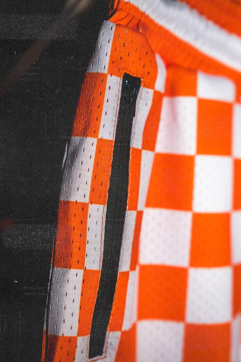 May include: Orange and white checkered fabric with a black zipper detail. The fabric has a subtle mesh texture.