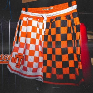 May include: Orange and black checkered basketball shorts with a white waistband and a white "T" on the left leg.