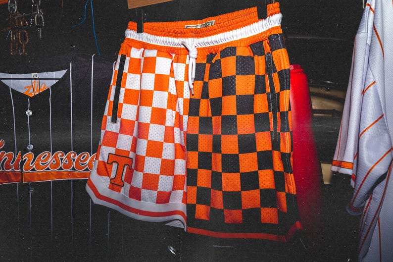 May include: Orange and black checkered basketball shorts with a white waistband and a white "T" on the left leg.