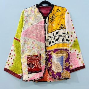 Może przedstawiać: Wielokolorowa kurtka patchwork z kwiatowymi i geometrycznymi wzorami. Kurtka ma długie rękawy, dekolt w serek i przednią kieszeń. Wisi na czarnym wieszaku. Projekt kurtki zawiera tekst "Maharajas Craft".