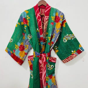 May include: A green floral print robe with a red interior, hanging on a wooden hanger. The robe features a colorful floral pattern with red, yellow, and blue flowers. The robe has a matching belt.