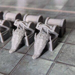 May include: A collection of miniature gray fantasy game pieces, including a figure, treasure chests, and quivers with arrows. The pieces are arranged on a tiled surface, suggesting a tabletop role-playing game setting.