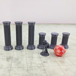 Puede incluir: Conjunto de miniaturas: pilares grises, una pequeña figura y un dado rojo de 20 caras. Los pilares, de diferentes alturas, tienen ranuras verticales. La figura parece ser un personaje con un bastón. Sobre un fondo cuadriculado.